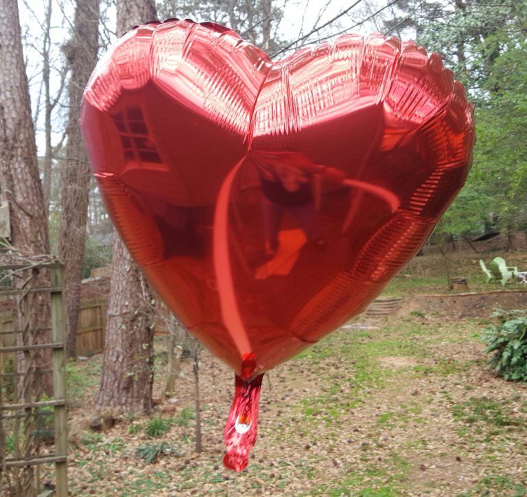 Red heart-shaped foil balloon in backyard